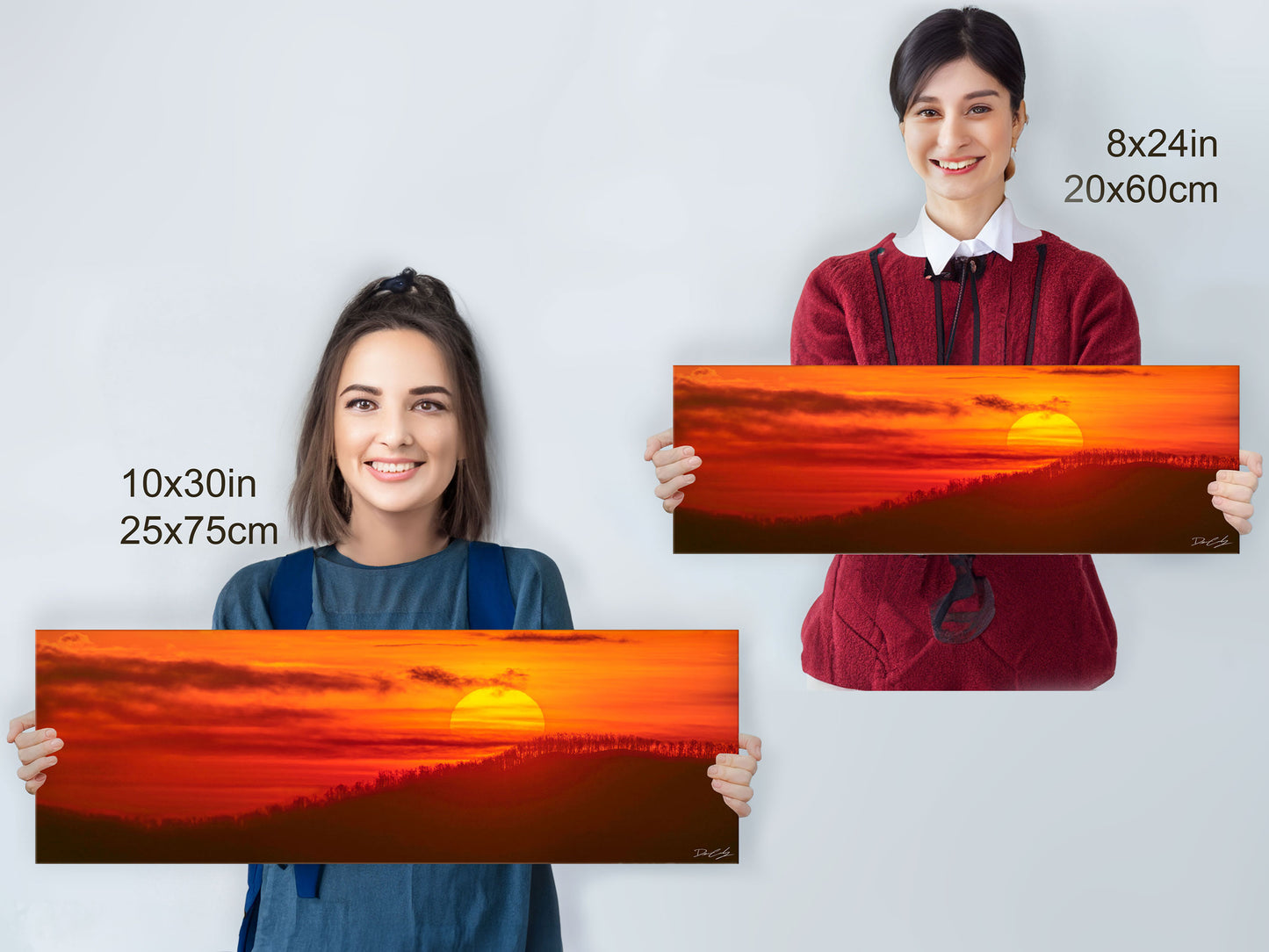 People holding Radiant Hope fine art prints in 10x30 inch and 8x24 inch sizes for scale reference, featuring a sunrise scene with brilliant colors over mountain ridges.