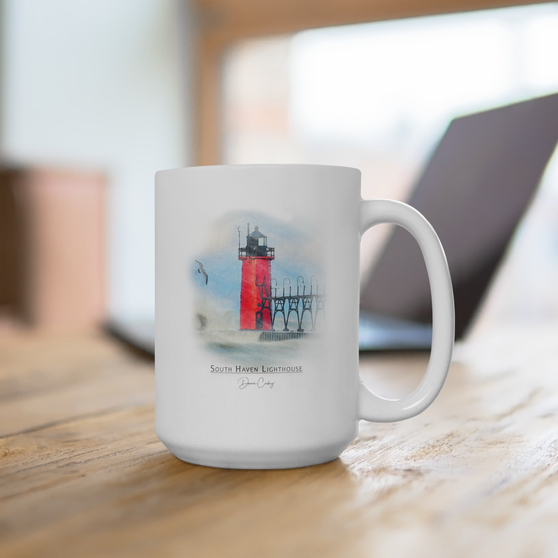 South Haven Lighthouse ceramic mug by Dennis Caskey sitting on a desk