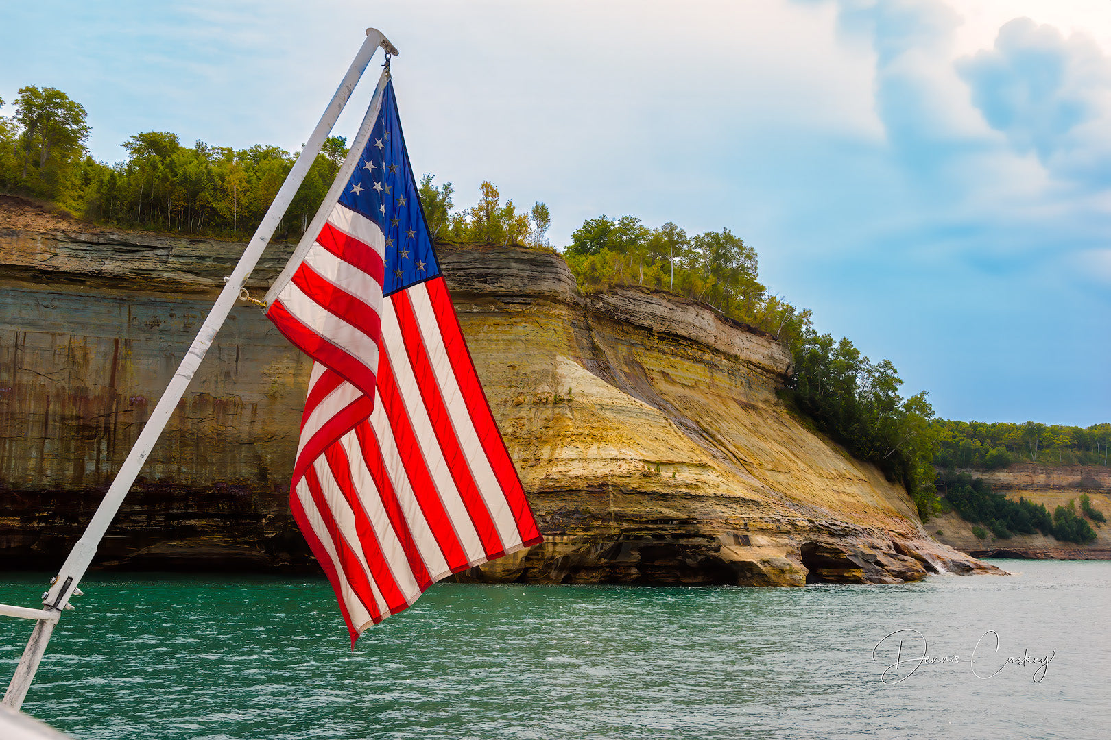 American flag hanging off the back of a boat on Lake Superior with Pictured Rocks National Lakeshore in the background.